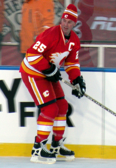 Un joueur de hockey en uniforme rouge et blanc patine sur la glace en attendant de recevoir une passe.  Il porte une tuque au lieu d'un casque