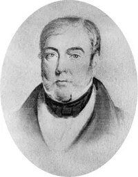 A portrait of an adult man with short, side-parted hair and a thick jacket