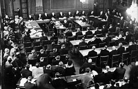 Le Procès en responsabilité de guerre en novembre 1945. Les membres du tribunal sont derrière la table en forme de fer à cheval, devant eux les secrétaires et les sténographes, derrière en trois rangées les accusés et leurs avocats. À gauche, le procureur, les représentants de la Commission de contrôle et des diplomates étrangers, au premier plan le public et les journalistes[1].