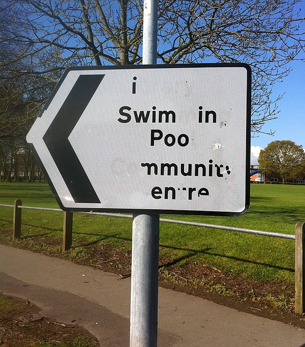 Vandalism on a street sign, making it read "i Swim in Poo"