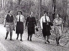 Czarno-białe zdjęcie pięciu kobiet w mundurach idących ścieżką w krzakach.