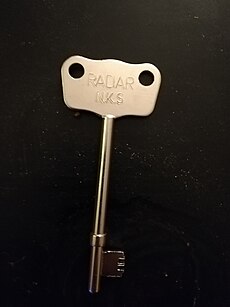 A large, silver-coloured key with a wide head is depicted on a dark-coloured background.On the head of the key, the text RADAR N.S.K is inscribed.