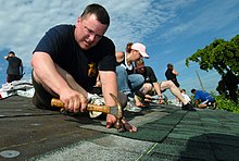 Collective installation of asphalt shingles, United States. US Navy 070706-N-3832S-057 Cyptologic Technician Technical 1st Class Jason Guidry nails shingles onto the roof of a house during a community relations project with Habitat for Humanity.jpg