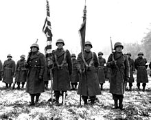 Two color guards and color bearers of the Japanese American 442nd Combat Team stand at attention while their citations are read. They are standing on the ground of Bruyeres, France, where many of their comrades fell. 442nd RCT citation presentation in Bruyeres 1944-11-12.jpg