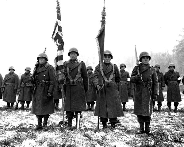 Two color guards and color bearers of the Japanese-American 442nd Combat Team stand at attention while their citations are read. They are standing on 