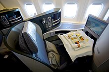 Airline business class cabin. Seats arranged in twos, with forward display screens.