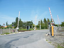 Blick auf den Bahnübergang (Barrieren erhöht) neben dem Bahnhof bei sonnigem Wetter.