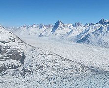 Photographie aérienne et en couleurs d'un glacier traversant une vallée encadrée de massifs montagneux.