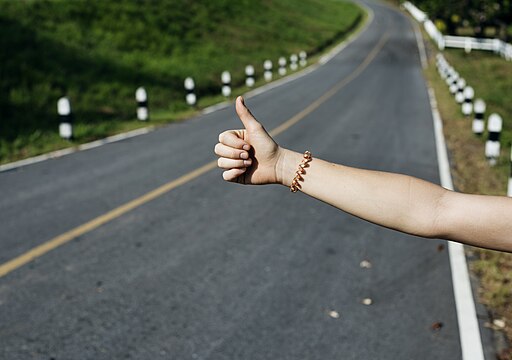 Hitch hiking sign near road (Unsplash)