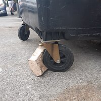 Improvised wooden chock used on a 4 wheeled plastic bin