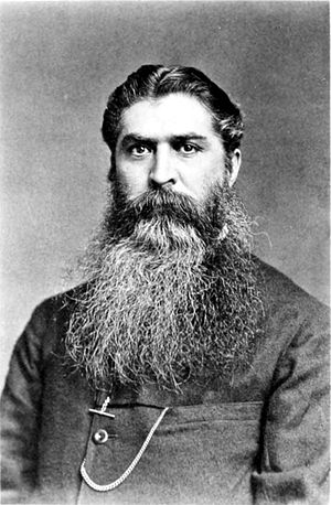 black and white photograph of a man with a large dark beard, streaked with white.