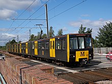 Yellow passenger train next to a stone wall