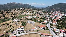 A color, aerial photograph of a village in the foreground with mountains in the background.