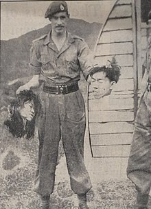 A Royal Marine holding the severed heads of suspected pro-independence fighters during the Malayan Emergency (1948-1960) 10th May 1952 - This Horror Must End.jpg