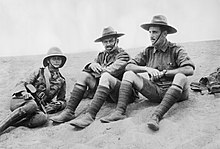 Portrait en noir et blanc de trois hommes en uniforme militaire, assis par terre.