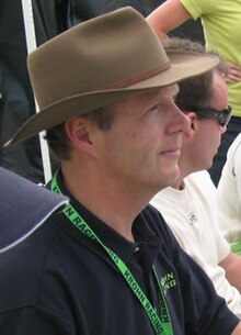 Photo de profil droit d'Eric van de Poele, portant un polo noir et un chapeau beige