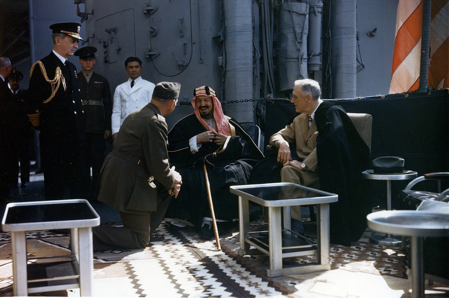 Le président Franklin Roosevelt en compagnie du roi Abdelaziz Al Saoud, du colonel William A. Eddy (en) (qui sert d'interprète, un genou au sol) et de l'amiral William Leahy (debout, à gauche) sur l'USS Quincy.