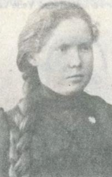 A young white woman with fair hair in a long braid, wearing dark, high collared clothes