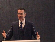 A middle aged white man in a suit at a lectern