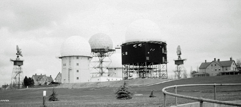 The foreground radome with dark-clad support structure houses a USAF AN/FPS-26A just completing construction c. late 1962 at the Missile Master military installation at Fort Lawton Air Force Station, which had a Direction Center in the nuclear bunker.  The two radars without radomes are US Army AN/FPS-6 heightfinders; the radome with an open steel grid support structure is an FAA search radar; and the two radars with radomes and white clad support structures are USAF AN/FPS-6A heightfinders.