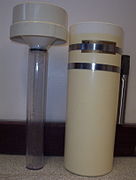 Standard rain gauge. On the right can be seen a overflow catch with a metal pipe that fits over a metal post in the ground. On the left is the funnel with the graduated cylinder attached.