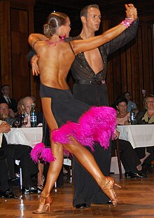 Latin dancers in their costumes. The woman is wearing a backless dress with deep slits on its lower portion, while the man is wearing a shirt with top buttons open. Tanzturnier 28.JPG