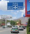 Placa trilingue (tibetano, mandarim e inglês) na entrada de Lhassa, a capital do Tibete. No centro, pode ser vista uma escultura dourada representando iaques, que são animais típicos do Tibete.