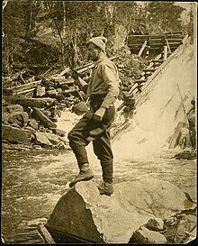 Thomson fishing at Tea Lake Dam in Algonquin Provincial Park, c. 1915/16 Tom Thomson, standing on a rock fishing in moving water.jpg