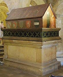 Na obrázku je vyfocena dřevěná tumba knížete Vratislava I. zdobená mnoha znaky včetně českého lva položená na kamenné bloku. Na její přední straně lze spatřit miniaturu samotného knížete Vratislava.