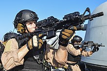 A United States Coast Guard Maritime Law Enforcement Specialist with an EOTech holographic sight and a magnifier on an M4 carbine. The pictured magnifier is flipped in, and is magnifying the view through the sight. USCG enforcement specialists on USS Monterey (CG-61) 2013.JPG