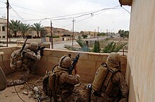 Two US Marines providing covering fire with a M4 carbine and a 40 mm M203 grenade launcher while a Marine from Air Naval Gunfire Liaison Company spots targets in Ramadi, Iraq, 2006. US Navy 060520-N-7497P-229 Cpl. Julius Mitchell, left, and Cpl. Jeremy Rugg, center, lay down covering fire while Cpl. Adam Gokey spots insurgent positions on his right and fires a grenade, seen traveling through the air, whil.jpg