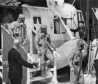 Armstrong, Aldrin és Collins kiszállnak a Helikopter 66-ból, izolációs öltözetet viselve, hogy azonnal átszálljanak egy karantén kocsiba a repülésüket követően