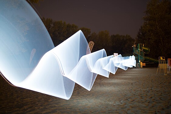 A wave painted with a white neon lamp in a flashlight, city beach in Płock, Poland.