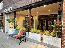 Entrance to a restaurant named Gai Noi. A rainbow colored bench is in front.