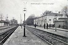 dentro de la estación con las vías, andenes, a la izquierda un refugio y a la derecha el edificio de pasajeros