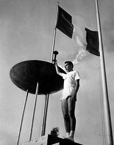 Giancarlo Peris lighting the 1960 Summer Olympics flame under the flag of Italy at Stadio Olimpico in Rome.