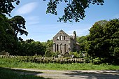 Foto van de ruïne van een klooster in een bosrijk landschap en bij een begraafplaats.