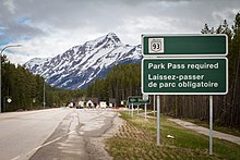 A sign at the park gates on the Icefields Parkway (Highway 93) advises tourists that they need to buy a pass to enter Jasper National Park in Alberta, Canada. Revenue collected from Park Passes goes to Parks Canada and helps fund the management of Canada's national parks. Jasper-Bear-Hunt-1.jpg