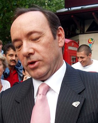 A close-up image of a man sporting a black suit and pink tie.