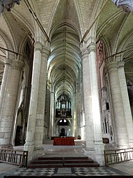 Intérieur d'une église avec des voûtes très hautes soutenues par des piliers en pierre. En haut de l'image, grand buffet d'orgue en bois. Au premier plan, 4 piliers.