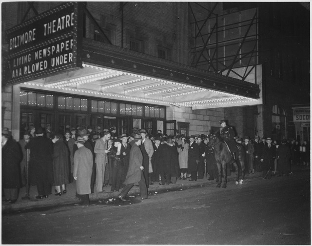 A crowd on the sidewalk in front of the lighted marquee of the Biltmore Theatre