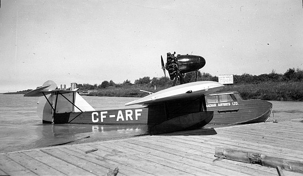 photo of single engine flying boat in the water, tied up at a wharf.