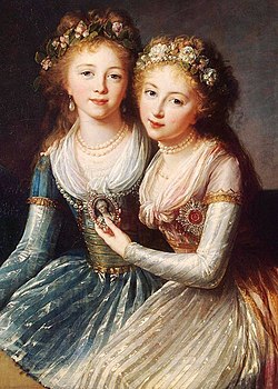 Two young girls embracing each other, wearing flower crowns. The older wears a light blue dress, the younger a yellow one, both with white lace and aprons. The younger holds a pendant with the portrait of a man in it.