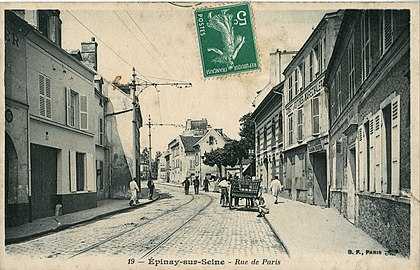 La rue de Paris dans les années 1900. Le tracé historique de la RN 14 est alors parcourue par le tramway Enghien - Trinité dont on voit les rails de la voie unique. C'est l'ancêtre du T8.