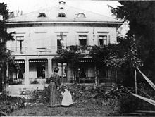Lydia Escher in weissem Kleidchen, etwa zweijährig neben Frau, die zur Villa Belvoir blickt, die im Hintergrund zu sehen ist. Schwarzweissfotografie, Querformat, um 1860