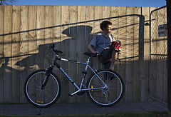 A boy with a bicycle against a wooden fence in the late afternoon, Auckland, New Zealand