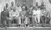 A black and white photo of 13 Christian Zulu men seated outside of a church