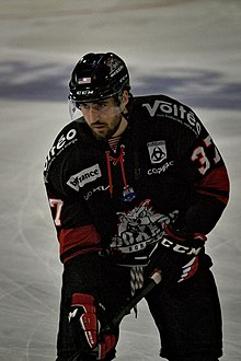 Joueur de hockey sur glace debout sur la glace, en équipement, regardant devant lui.