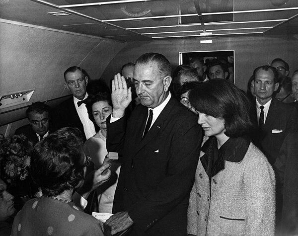 Cecil Stoughton's photograph of Lyndon B. Johnson being sworn in as President as Air Force One prepares to depart Love Field in Dallas. Jacqueline Kennedy (right), still in her blood-spattered clothes (not visible here), looks on.