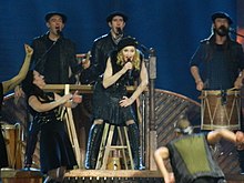 Madonna, flanked by Basque band Kalakan, singing "Open Your Heart" during 2012's The MDNA Tour. MDNA DSCN3395 (7603304574) (cropped).jpg